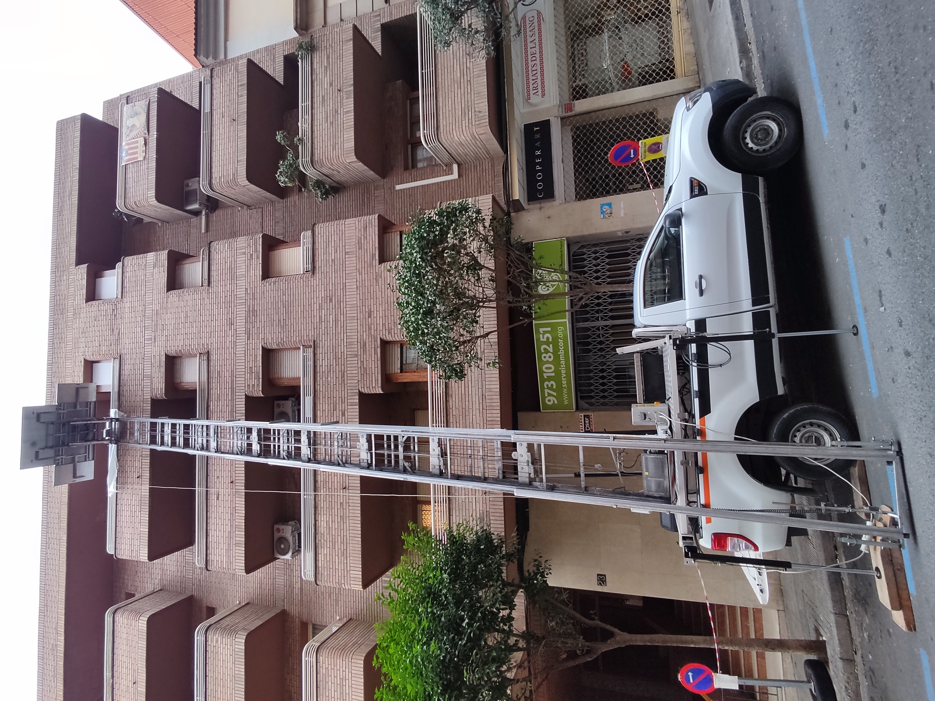 Camió grua de Mudances Sabaté davant bloc de totxo amb cartell Cooperart